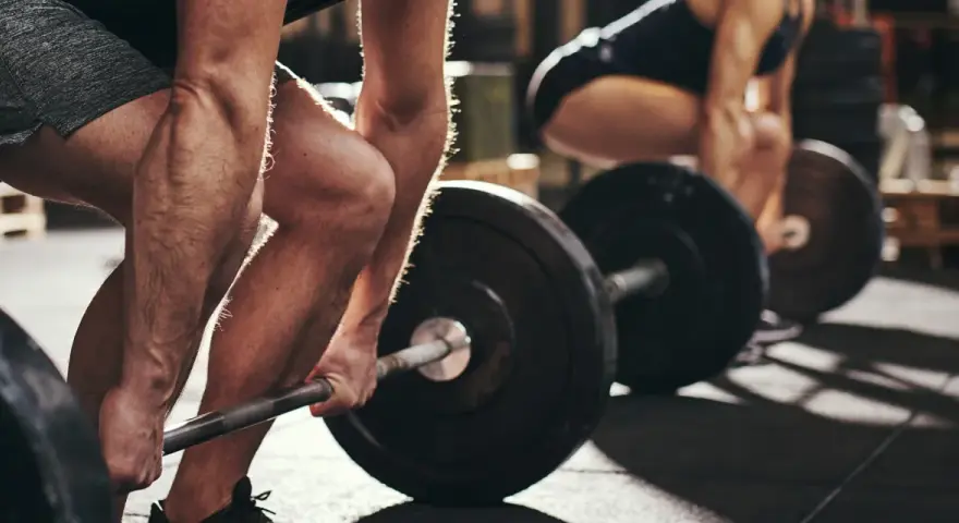 Personer lyfter skivstång i gym. Frågan "hur lång tid tar det att bygga muskler" besvaras med konsekvent träning.