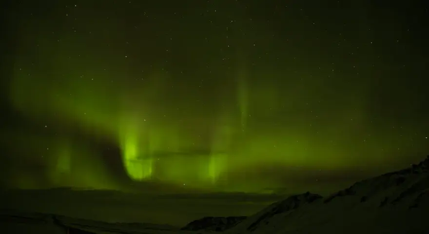 Niesamowita zorza polarna nad Islandią. Zielone smugi tańczą na nocnym niebie, oświetlając ośnieżony krajobraz i drogę.