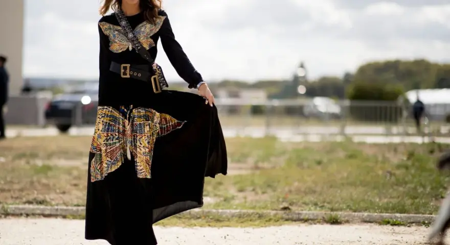 Mujer con vestido largo negro con estampado de mariposas, cinturón ancho y botines. Un ejemplo de como llevar un vestido largo informal con estilo.