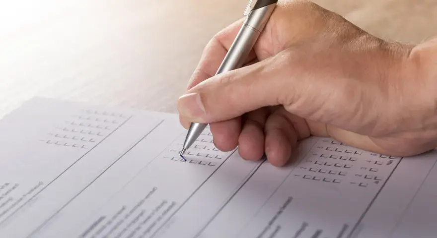 Dłoń z długopisem wypełnia formularz, zaznaczając odpowiedzi. To część procesu tworzenia wykazu majątku.