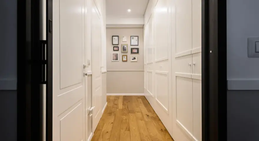 Corridoio con parquet e armadi bianchi. Un'idea per come dividere un corridoio lungo con porte e quadri decorativi.