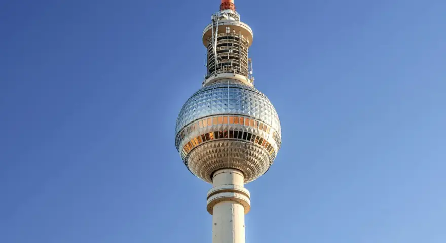 Die Torre della televisione di Berlino ragt in den blauen Himmel. Ihre kugelförmige Spitze mit Fenstern reflektiert das Licht.