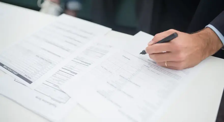 Ręka klienta podpisuje dokumenty ubezpieczeniowe. Agent ubezpieczeniowy czeka na zakończenie formalności.
