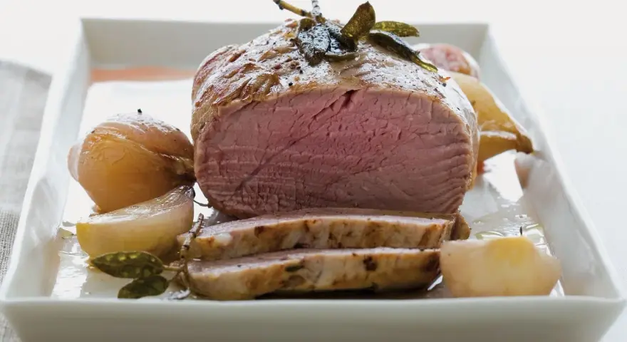 Succulento filetto al forno, cotto alla perfezione con cipolle e erbe aromatiche, servito su un piatto bianco.