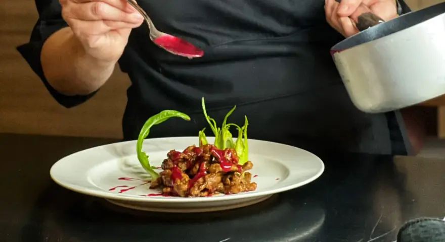 Chef decora un piatto di straccetti di manzo con una salsa rossa brillante, guarnendo con verdure verdi.