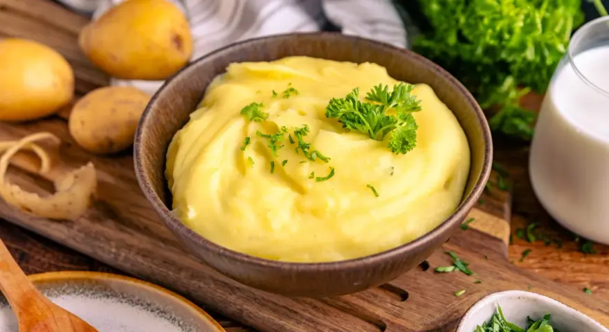 Cremiger Kartoffelbrei, perfekt zubereitet im Thermomix, garniert mit Petersilie. Dazu frische Kartoffeln und ein Glas Milch.