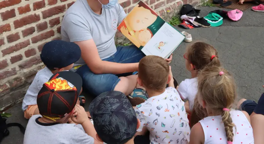 Un animateur lit un livre illustré à des enfants assis en cercle. L'image évoque un moment de partage et d'apprentissage, comme un diplôme animation.