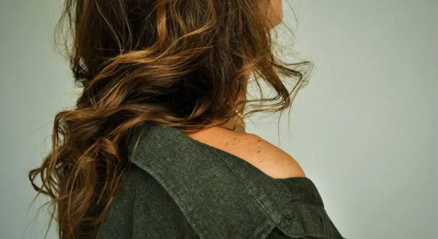 Spalle scoperte e capelli castani mossi, un dettaglio di donne con pochi capelli che incornicia il volto.