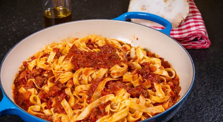 Herzhafte Tagliatelle mit einer reichhaltigen alla bolognese Sauce in einer blauen Pfanne, bereit zum Servieren.