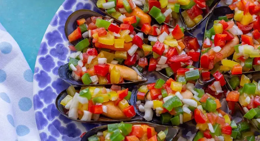 Mejillones a la vinagreta, cubiertos con una colorida mezcla de pimientos y cebolla picados. Un plato fresco y vibrante.