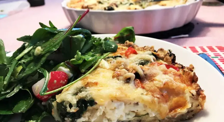 En bit krämig vegetarisk paj med ost och grönsaker, serverad med en fräsch sallad.