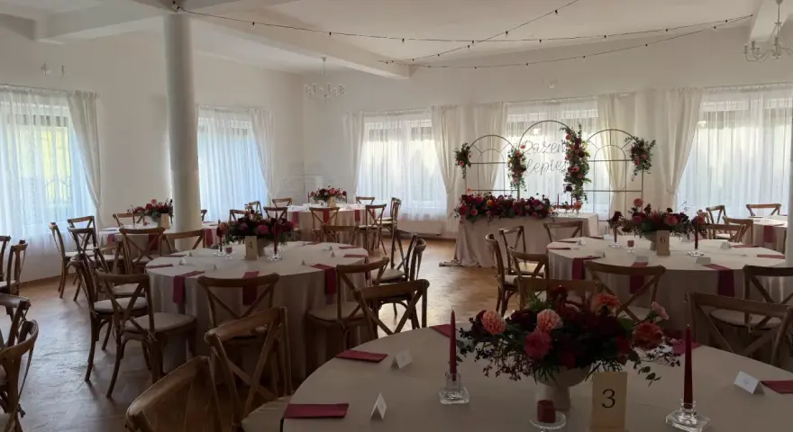 Elegancka sala weselna z okrągłymi stołami, kwiatami i świecami. Idealne miejsce, by wybrać najlepszą salę na wesele.