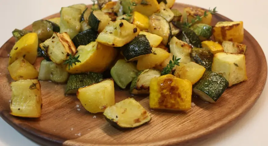 Délicieux courgettes au four, coupées en dés et parsemées de thym frais sur un plat en bois.