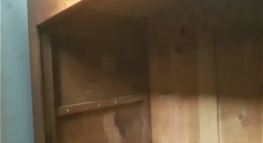 Intérieur d'une armoire ancienne en bois, prête à démonter. Les étagères sont visibles, ainsi que les marques du temps.