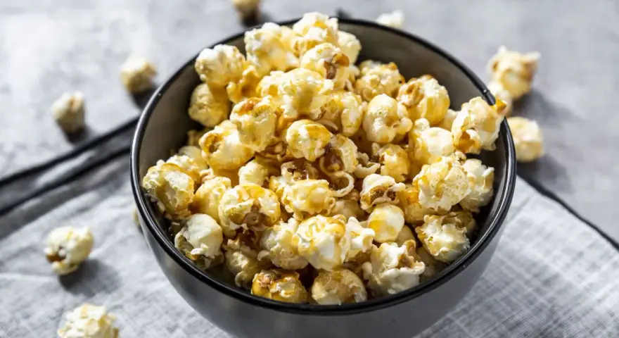 Un bol rempli de pop corn sucré, avec quelques grains éparpillés autour. Un délice croustillant pour une soirée cinéma.