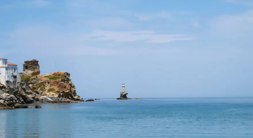 Widok na morze z latarnią morską na skale i zabudowaniami na klifie na wyspie Andros.
