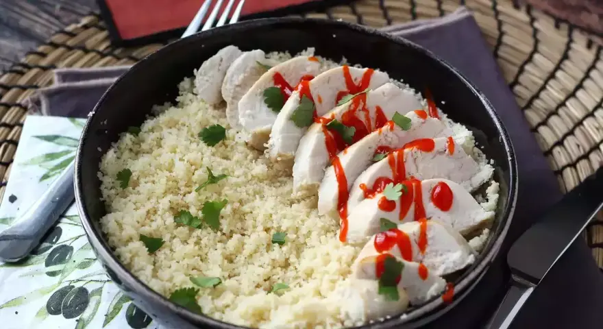 Delizioso petto di pollo in padella, affettato e servito su un letto di couscous, guarnito con prezzemolo e un filo di salsa piccante.