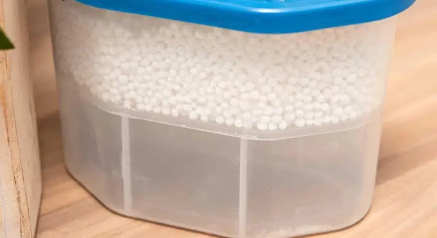 Luftentfeuchter Granulat wird hart, wenn es Feuchtigkeit aufnimmt. Der Behälter zeigt, wie das Granulat die Luft trocknet und sich unten Wasser sammelt.
