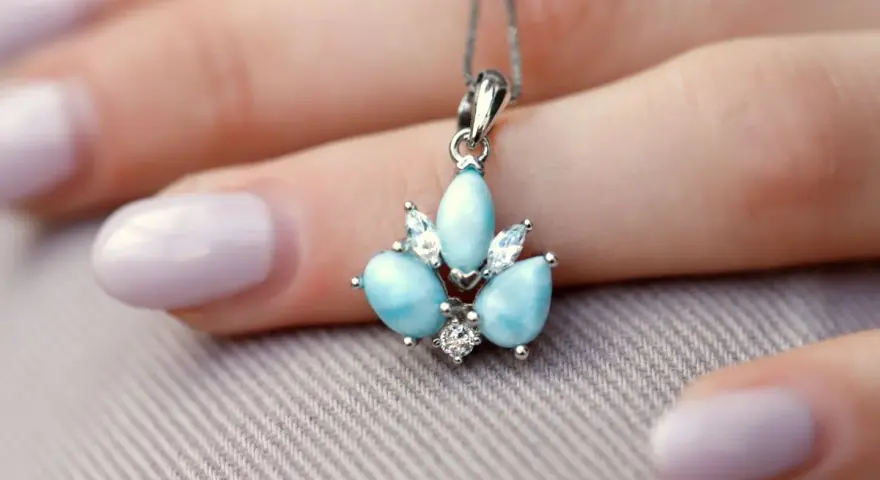 Un ciondolo con una splendida larimar pietra, incastonata con zirconi, adagiato su una mano con unghie lilla.