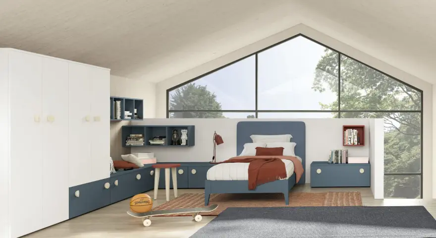 Un accogliente **letto sotto la finestra** in una stanza moderna, con armadio bianco, librerie blu e un pallone da basket.