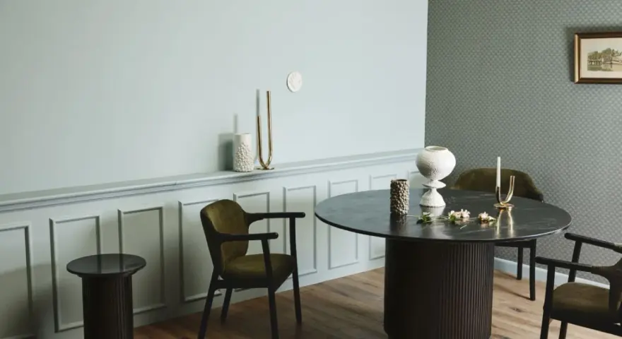 Ett runt matbord med mörka stolar skapar en inbjudande atmosfär. Utrymme runt matbordet ger plats för samtal och gemenskap.