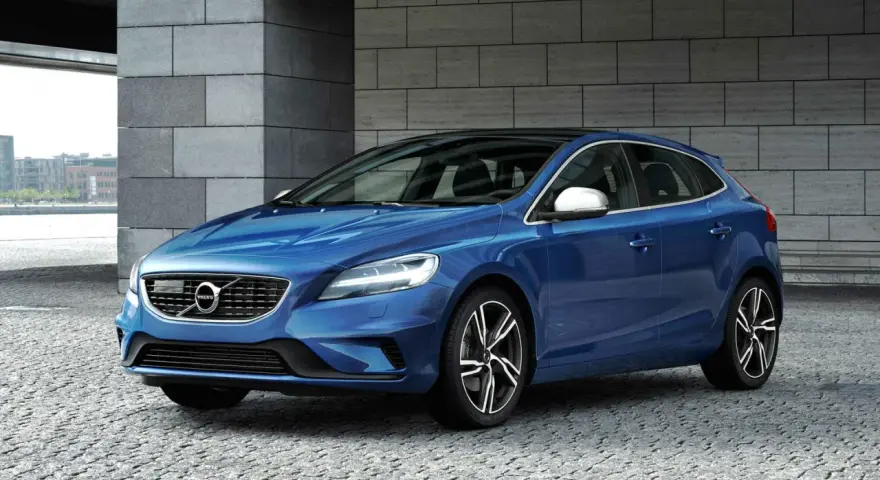 Niebieskie Volvo V40 D2 z czarnym dachem, zaparkowane na kamiennej nawierzchni, z nowoczesną architekturą w tle.