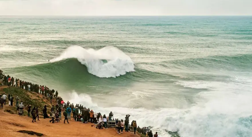 Riesige Welle bricht vor Zuschauern am mole strand. Ein Surfer reitet die Welle.