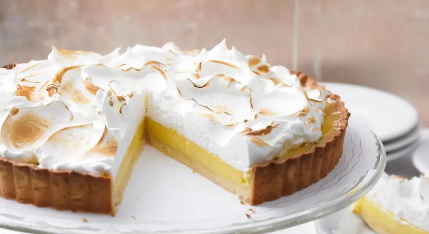 Eine köstliche Tarte au Citron mit fluffiger Baiserhaube, die auf einem Tortenständer präsentiert wird.