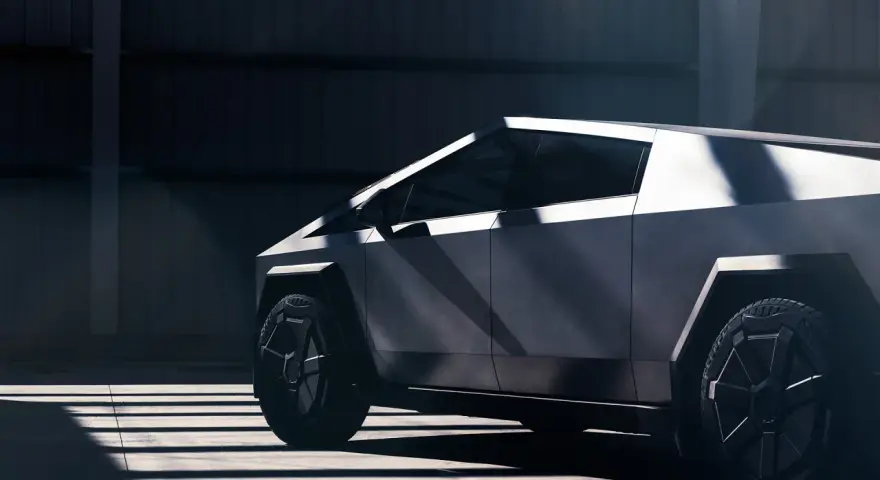 Tesla Cybertruck w ciemnym wnętrzu, widok z boku, podkreślony przez światło i cień.
