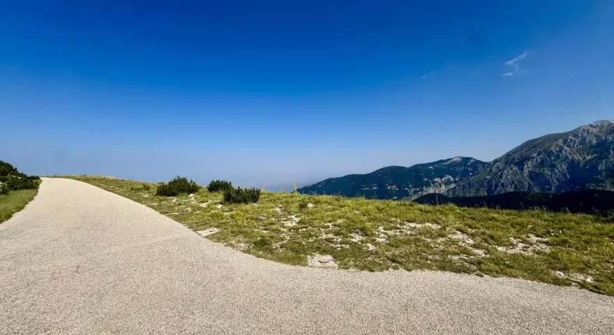 Sentiero ghiaioso verso la cima Blockhaus, con prati verdi e montagne sullo sfondo sotto un cielo azzurro.