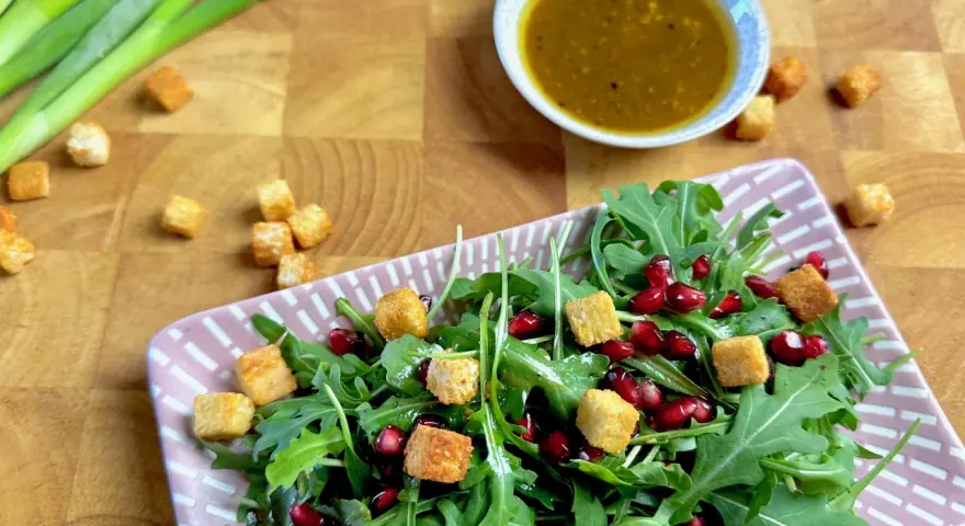 Frischer Rucola Salat mit Granatapfelkernen und Croutons, dazu ein Dressing.