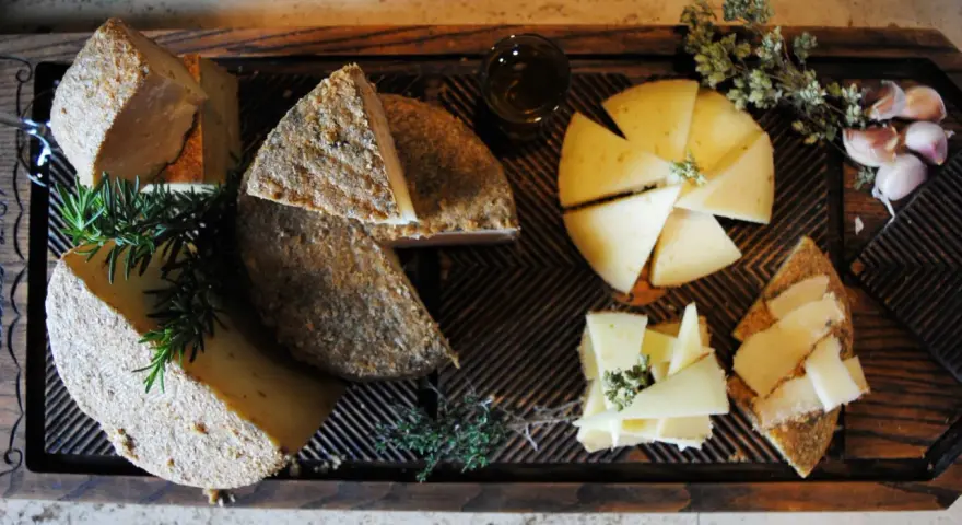 Tabla de quesos variados, hierbas aromáticas y ajos sobre madera.