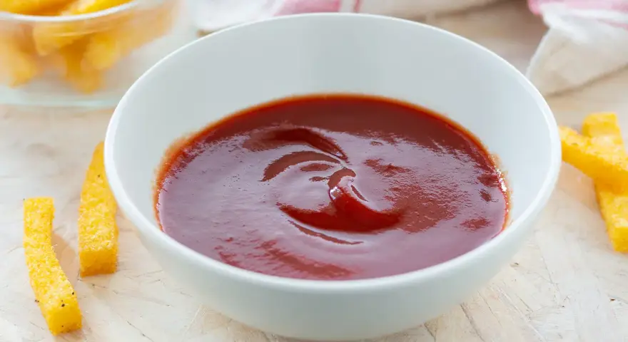 Una ciotola di ketchup fatto in casa, pronto per intingere bastoncini di polenta dorati.