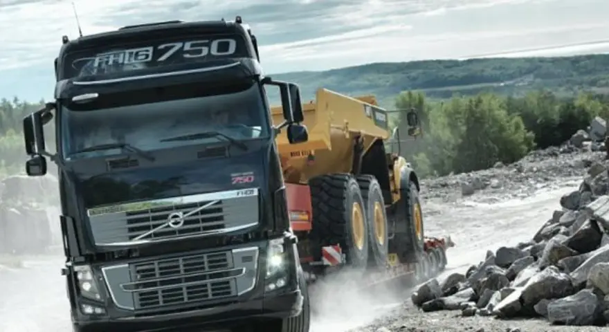 Ciężarówka Volvo FH16 750 z naczepą przewozi żółty wozidło przegubowe przez kamieniołom.