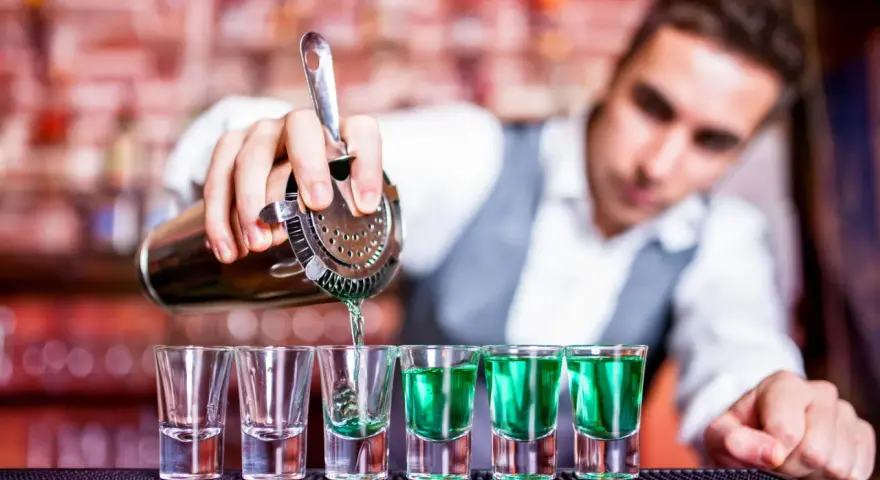 Barman nalewa zielony alkohol do kieliszków.