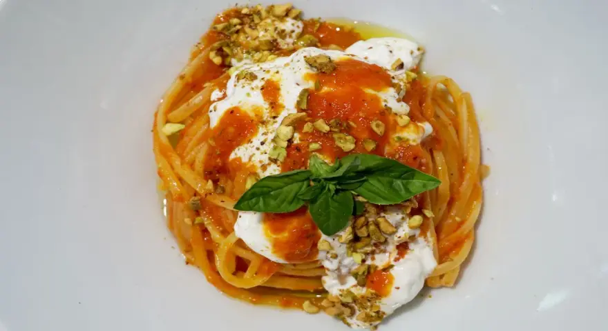 Un piatto invitante di pasta con stracciatella, salsa di pomodoro, pistacchi tritati e una foglia di basilico fresco.
