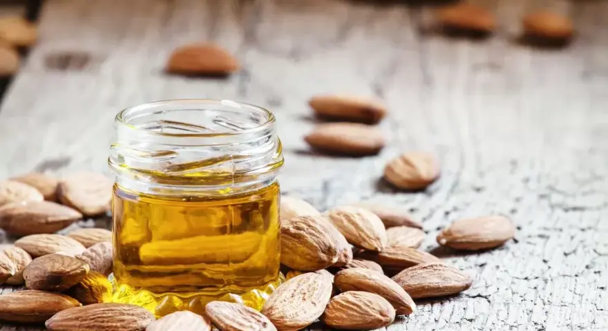 Aceite de almendras para que sirve: un frasco de aceite dorado rodeado de almendras sobre madera rústica.