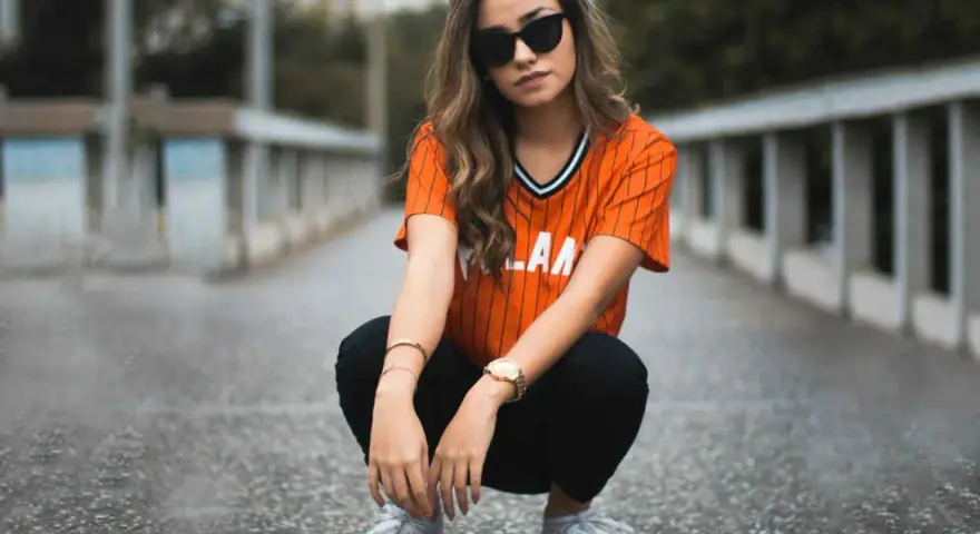 Mujer con estilo smart casual, con camiseta naranja a rayas, pantalones negros y zapatillas deportivas.