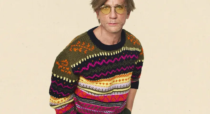 Mann mit gelber Brille trägt einen bunten Pullover aus Wolle, schleudern von Mustern.