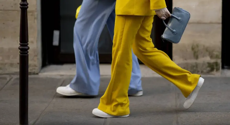 Un outfit tailleur con sneakers, giallo brillante e azzurro polvere, camminano sul marciapiede.