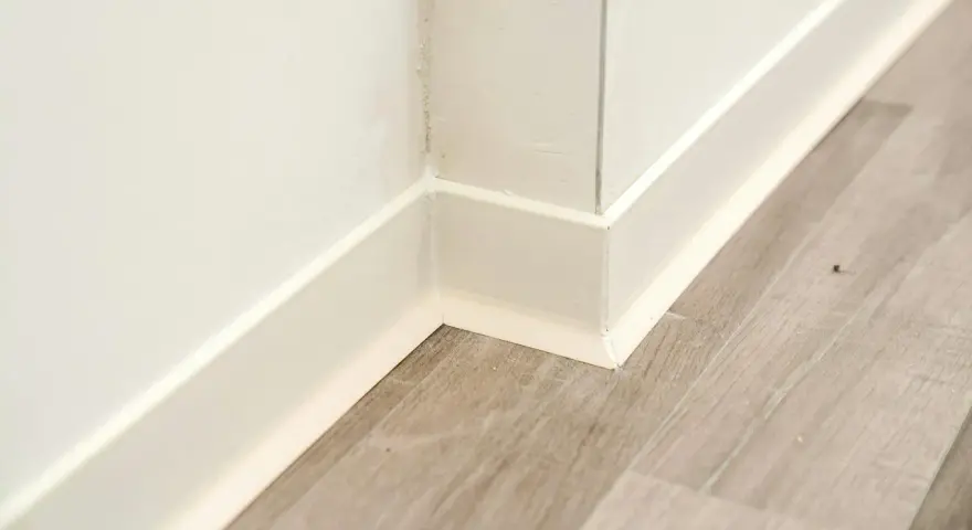 Angolo di una stanza con parquet grigio e battiscopa bianco appena installato.