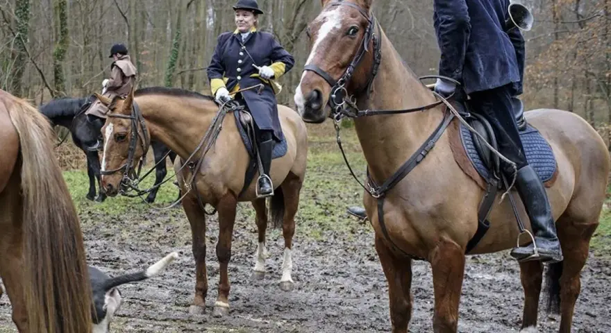 Cavaliers en tenue de chasse à courre, prêts pour l'aventure dans la forêt boueuse.