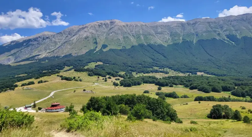 Vasta distesa verde ai piedi del monte Mileto, con un edificio circolare rosso e una strada tortuosa.