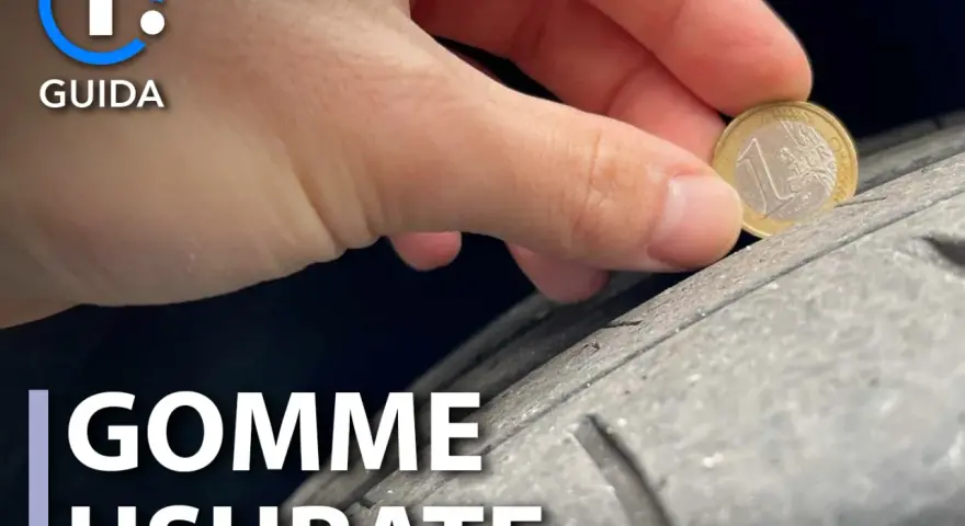 Una mano tiene una moneta da 1 euro per controllare il battistrada di pneumatici usurati. La guida mostra come verificare la sicurezza.