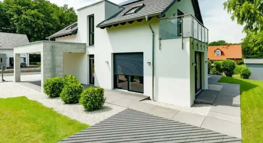 Nowoczesna, biała elewacja budynku z betonowym zadaszeniem, szarymi roletami i szklanym balkonem.