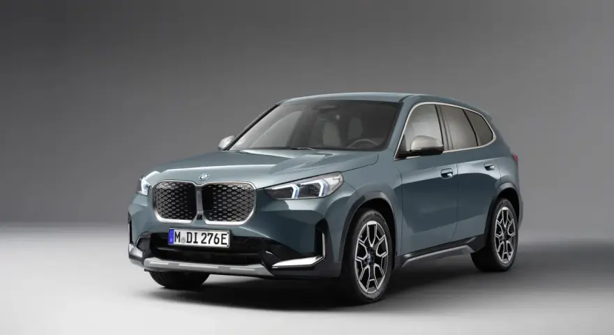 BMW iX1 w kolorze zielonym, widok z przodu, na szarym tle.