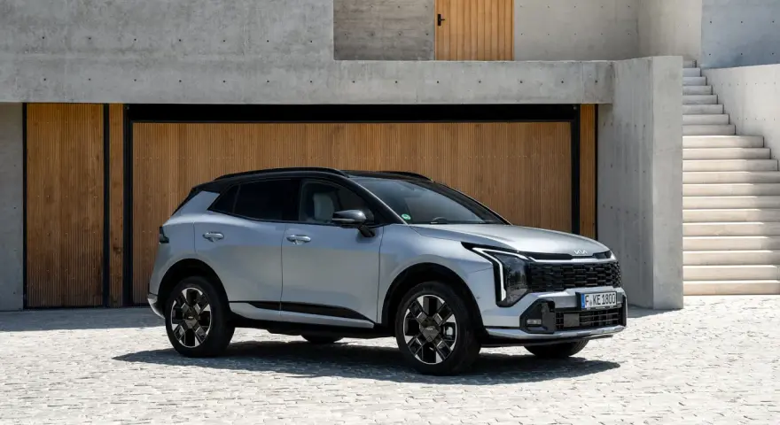 Elegancki, srebrny Kia Sportage Hybrid z czarnym dachem zaparkowany przed nowoczesnym budynkiem z drewnianymi drzwiami i betonowymi schodami.