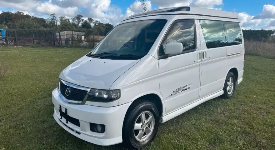 Biały van Mazda Bongo z podnoszonym dachem, zaparkowany na trawie.