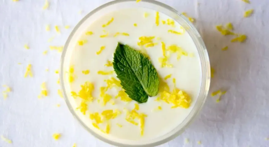 Delicioso mousse de limón, adornado con ralladura de limón y una hoja de menta fresca, servido en un vaso transparente.