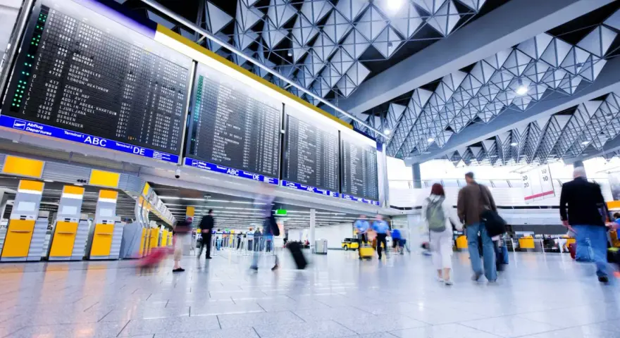 Tablica odlotów na lotnisku, ludzie z bagażami spieszą na boarding.